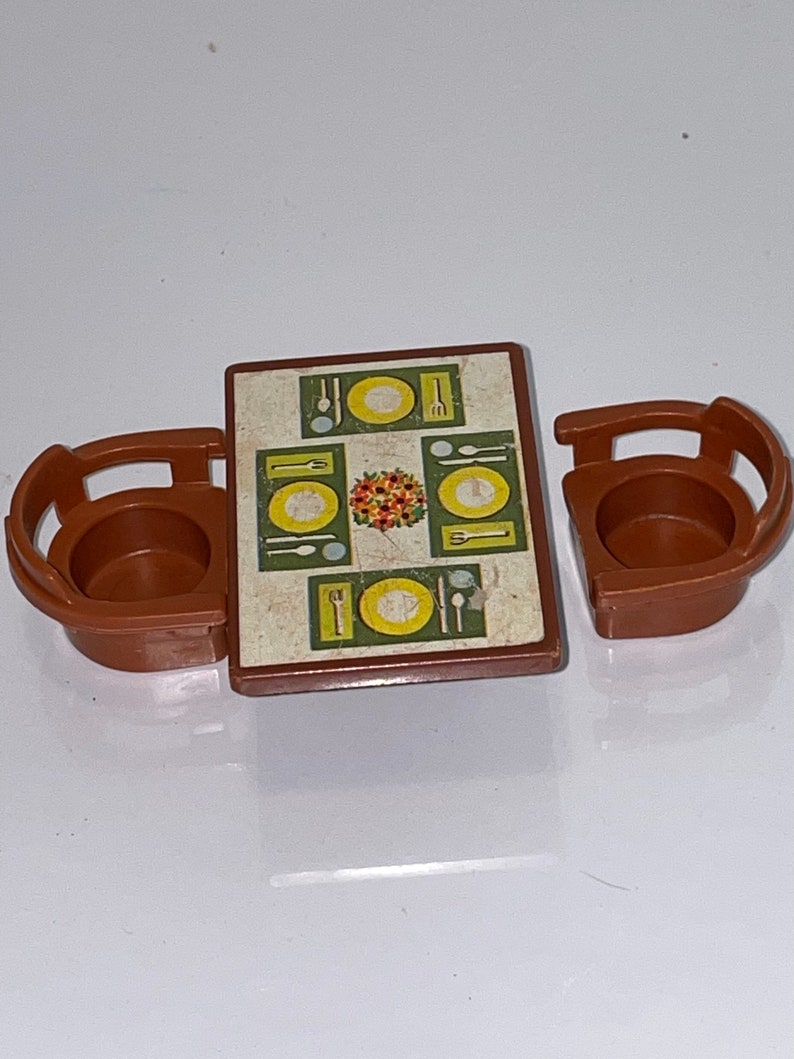 May include: A brown plastic toy table and two chairs. The table has a green and yellow patterned tabletop with a floral design and images of plates, forks, knives, and spoons.