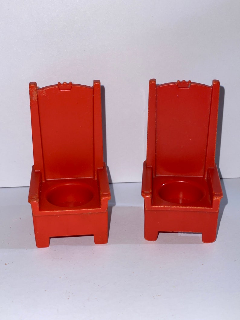 May include: Two red plastic chairs with a crown design on the back. The chairs have a small round seat.