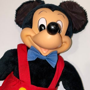 May include: A plush Mickey Mouse toy with black fur, large ears, and a red and yellow jumpsuit. The toy has a blue bow tie and a friendly expression.