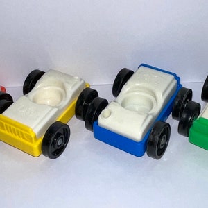 May include: Four toy cars in red, yellow, blue, and green. Each car has a white top with a small hole in the center. The cars have black wheels.