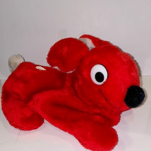 May include: Red plush toy rabbit with a white eye and black nose. The rabbit is lying on its side with its head turned to the right.