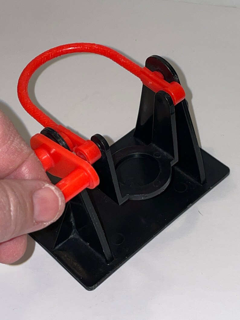 May include: A black plastic toy with a red rubber band and a red plastic handle. The toy is designed to launch a small object.