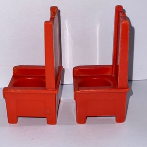 May include: Two orange plastic chairs with a simple design. The chairs have a rounded seat and a high back.