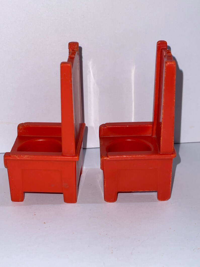 May include: Two orange plastic chairs with a simple design. The chairs have a rounded seat and a high back.