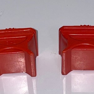 May include: Two red plastic blocks with a raised X design on the top. The blocks are about 2 inches tall and 2 inches wide.