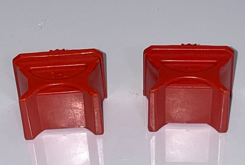 May include: Two red plastic blocks with a raised X design on the top. The blocks are about 2 inches tall and 2 inches wide.
