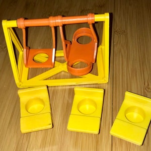 May include: A vintage yellow and orange plastic toy swing set with three yellow seats. The swing set is made of plastic and has a simple design.