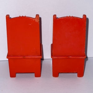 May include: Two orange plastic chairs with a simple design. The chairs have a high back and a seat with a small ledge. The chairs are made of a smooth plastic.