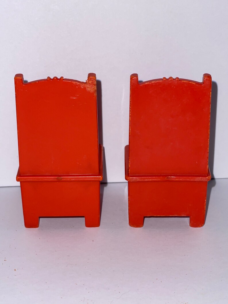 May include: Two orange plastic chairs with a simple design. The chairs have a high back and a seat with a small ledge. The chairs are made of a smooth plastic.
