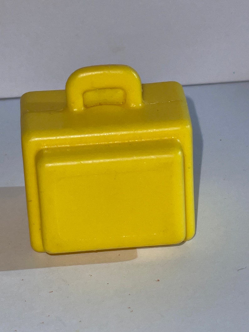 K&ouml;nnte beinhalten: Ein gelber Plastik-Spielzeugkoffer mit einem Griff oben. Der Koffer ist ein kleines Spielzeug f&uuml;r Kinder.