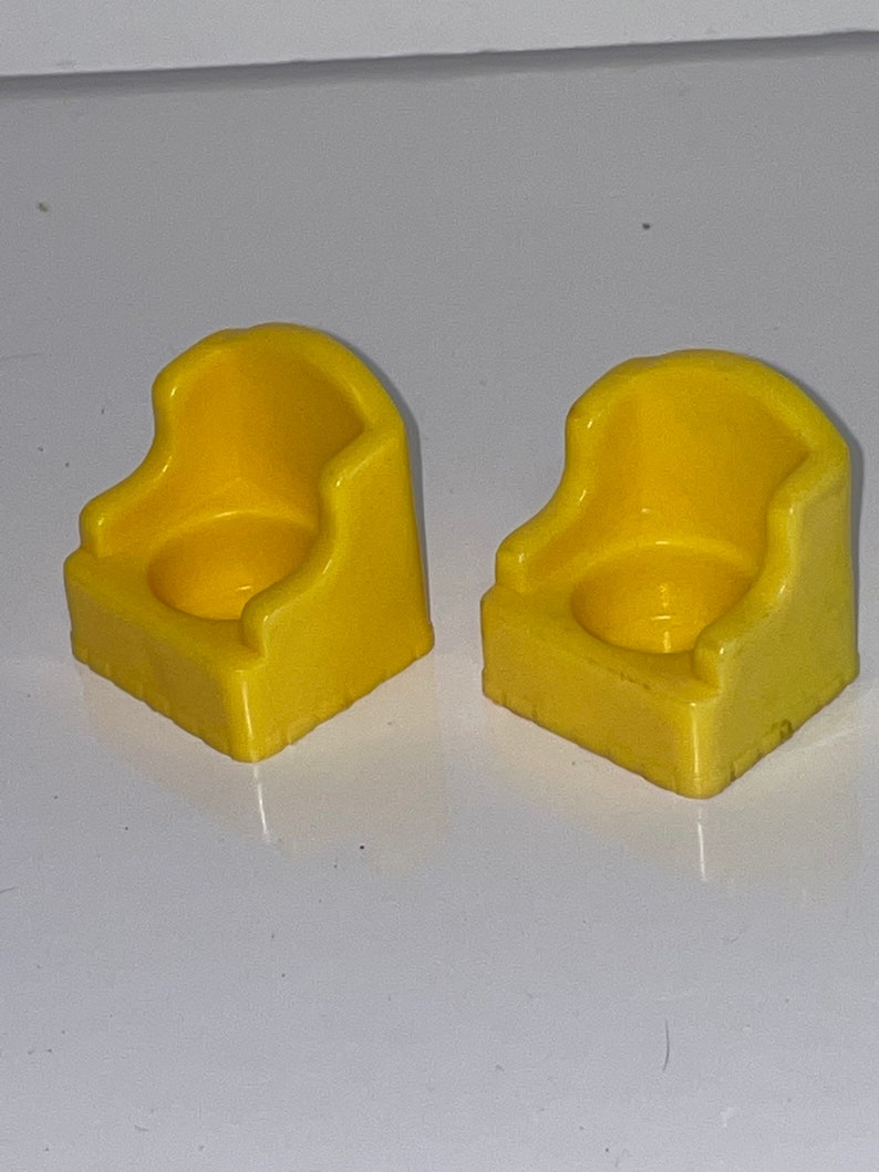 May include: Two yellow plastic chairs with a rounded back and a small seat. The chairs are designed for small children.