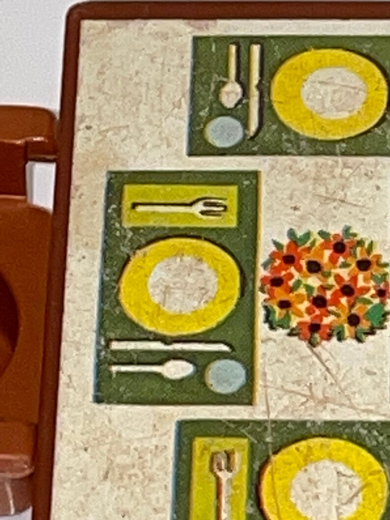 May include: A brown wooden table with a white and green patterned tabletop. The tabletop has a design of plates, forks, knives, spoons, and a floral centerpiece.