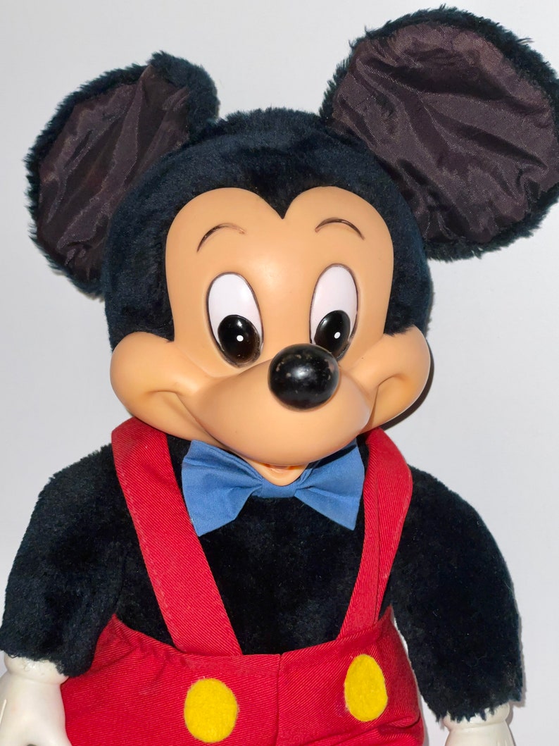 May include: A plush Mickey Mouse toy with black fur, large ears, and a red and yellow jumpsuit. The toy has a blue bow tie and a friendly expression.
