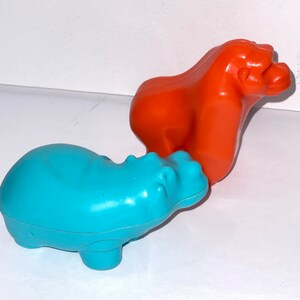 May include: A blue plastic hippopotamus toy and an orange plastic gorilla toy. Both toys are made of a smooth, shiny plastic.