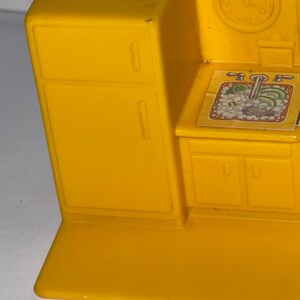 K&ouml;nnte beinhalten: Gelbes Spielzeug-K&uuml;chenset aus Plastik mit einem K&uuml;hlschrank, einer Sp&uuml;le und Schr&auml;nken. Die Sp&uuml;le hat einen Aufkleber mit einem Wasserhahn und Gem&uuml;se.