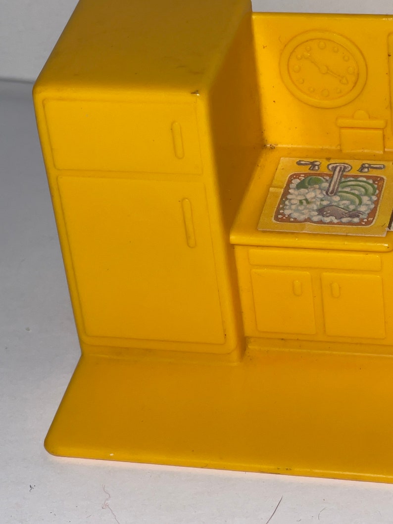 K&ouml;nnte beinhalten: Gelbes Spielzeug-K&uuml;chenset aus Plastik mit einem K&uuml;hlschrank, einer Sp&uuml;le und Schr&auml;nken. Die Sp&uuml;le hat einen Aufkleber mit einem Wasserhahn und Gem&uuml;se.