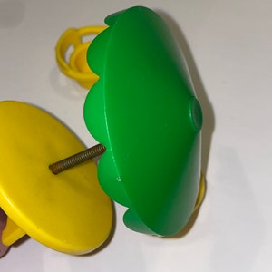 May include: A green plastic toy umbrella with a yellow base and a metal screw. The umbrella has a scalloped edge and is designed for a dollhouse or playset.