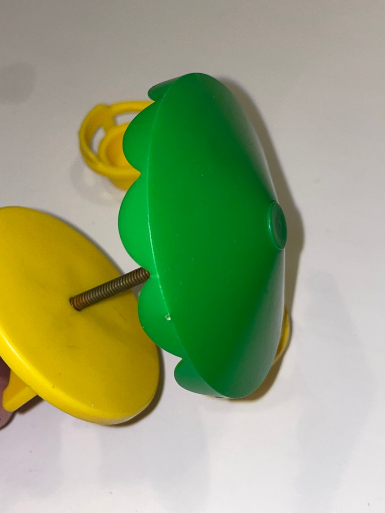 May include: A green plastic toy umbrella with a yellow base and a metal screw. The umbrella has a scalloped edge and is designed for a dollhouse or playset.