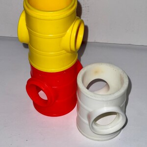 May include: Three plastic toy fire hydrants stacked on top of each other. The top hydrant is yellow, the middle hydrant is red, and the bottom hydrant is white.