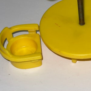 May include: A yellow plastic toy table and chair set with a green umbrella. The table has a round top and three legs. The chair has a back and a seat.