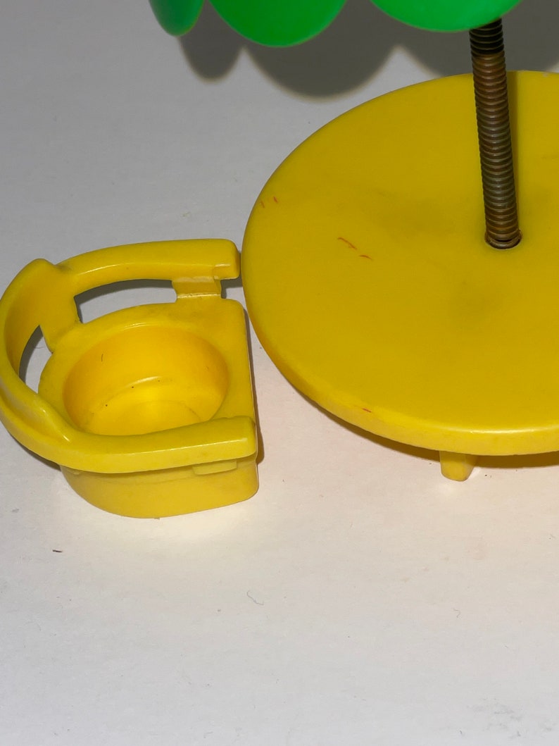May include: A yellow plastic toy table and chair set with a green umbrella. The table has a round top and three legs. The chair has a back and a seat.