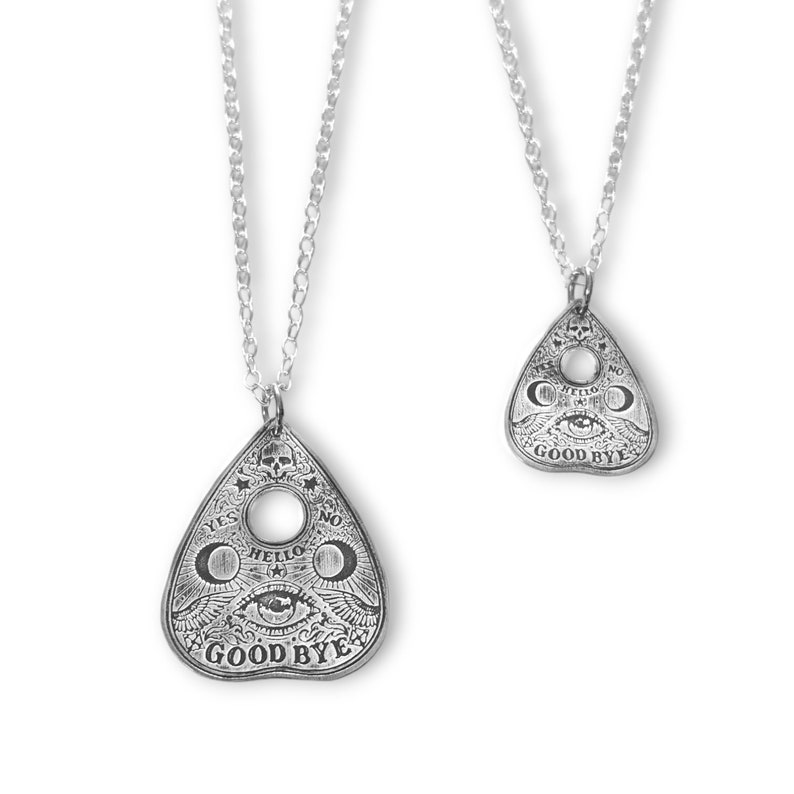 Two silver necklaces with planchette pendants. The larger pendant has the words "YES", "NO", "HELLO", and "GOODBYE" inscribed on it. The smaller pendant has the words "YES", "NO", "HELLO", and "GOODBYE" inscribed on it.