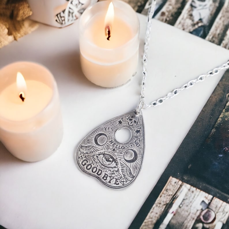 Silver pendant necklace featuring a Ouija board planchette design with the words "Yes", "No", "Hello", "Goodbye" and a stylized eye.
