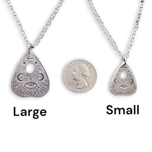 Two silver necklaces with a Ouija board planchette pendant. The larger pendant is larger than the size of a quarter. The smaller pendant is about the size of a quarter. The necklaces are on a white background.