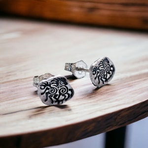 May include: A pair of silver stud earrings with a black horse design. The horse is stylized and has a swirling pattern.