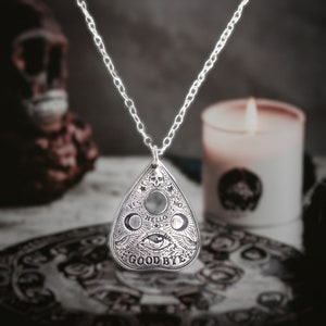 Silver necklace with a silver pendant shaped like a Ouija board planchette. The pendant has the words "Yes", "No", "Hello", "Goodbye" and an eye design.