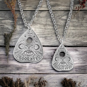 Two silver necklaces with Ouija board planchette pendants. Each pendant features the words "Yes", "No", "Hello", "Goodbye", and a crescent moon with an eye in the center.