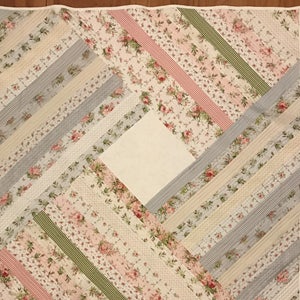 May include: A quilt with a diamond pattern made from strips of fabric in shades of pink, green, white, and blue. The fabric has floral patterns.