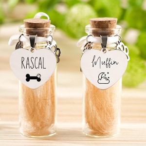 Pode incluir: Duas pequenas garrafas de vidro com rolhas, cada uma contendo uma substância castanha clara. Cada garrafa tem uma etiqueta em forma de coração com o nome de um animal de estimação, "Rascal" e "Muffin", e um ícone relacionado.