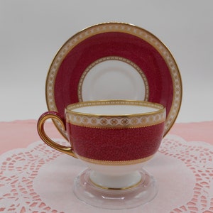 May include: A red and gold teacup and saucer set with a delicate floral pattern. The cup and saucer are made of fine china and have a glossy finish.