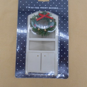 May include: A white wooden dollhouse hutch with a green and red Christmas wreath on the top. The packaging has a blue background with white polka dots and the text "T'was the night before..."