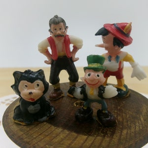 May include: A set of four vintage plastic figurines, including a black cat, a man with a red vest, a man with a green hat, and a man with a red hat and a long nose.