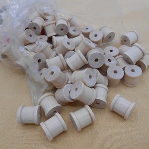 May include: A collection of small, unfinished wooden spools, each with a central hole. The spools are cylindrical with slightly flared ends. They are contained in a clear plastic bag, with some spools scattered outside.