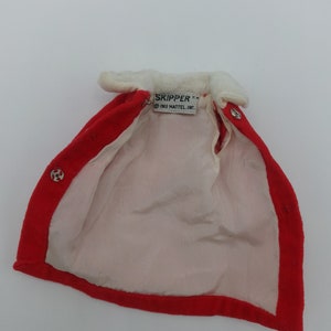 May include: Red velvet doll cape with a white faux fur collar and a white label that reads "SKIPPER TM 1963 MATTEL, INC."