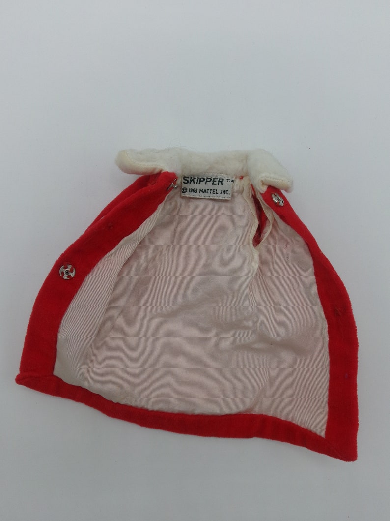 May include: Red velvet doll cape with a white faux fur collar and a white label that reads "SKIPPER TM 1963 MATTEL, INC."
