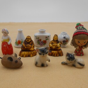 May include: A collection of miniature figurines including a wooden mouse, two ceramic cats, a ceramic woman in a red dress, a ceramic doll with a red and white hat, two ceramic vases with floral designs, and two ceramic Buddha figurines.