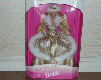 May include: A Barbie doll wearing a white fur-trimmed gold gown with a crown and a white fur stole. The doll is in a pink box with the words "Winter Fantasy Barbie" on the front.