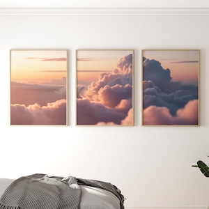 Puede incluir: Tres impresiones enmarcadas que muestran un paisaje de nubes al atardecer. La obra de arte presenta suaves tonos rosas, naranjas y azules, con nubes esponjosas que llenan el cielo. Los marcos tienen un acabado dorado, añadiendo un toque de elegancia a la serena escena.