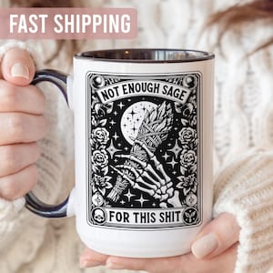 May include: White ceramic mug with a black rim and handle, featuring a black and white graphic design. The design includes a skeleton hand holding a bundle of sage, a moon, and the text "NOT ENOUGH SAGE FOR THIS SHIT."