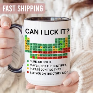 May include: White ceramic mug with a black handle and rim, featuring the text "CAN I LICK IT?" above a periodic table design. Below the text are colour-coded statements: "SURE, GO FOR IT", "MAYBE, NOT THE BEST IDEA", "PLEASE DON'T DO THAT", and "SEE YOU ON THE OTHER SIDE".