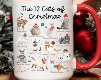 May include: A white ceramic mug with a red interior and handle, featuring the text "The 12 Cats of Christmas" and illustrations of various cat breeds wearing Santa hats. The mug is surrounded by festive holiday decorations.