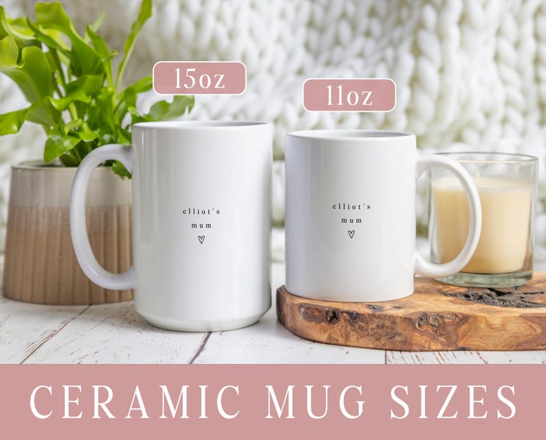 May include: Two white ceramic mugs with the text "elliot's mum" and a heart symbol. The larger mug is labeled "15oz" and the smaller mug is labeled "11oz". The mugs are on a white wooden surface. The text "CERAMIC MUG SIZES" is at the bottom.