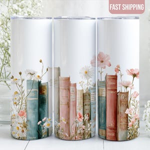 May include: White tumbler with a floral and book design. The design features a row of vintage books in teal, pink, and beige, with daisies and pink flowers. A great gift for book lovers.