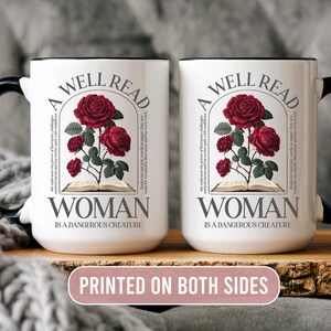 May include: Two white ceramic mugs with black handles and rims. Each mug features a design with red roses, an open book, and the text "A WELL READ WOMAN IS A DANGEROUS CREATURE". The phrase "PRINTED ON BOTH SIDES" is also visible.