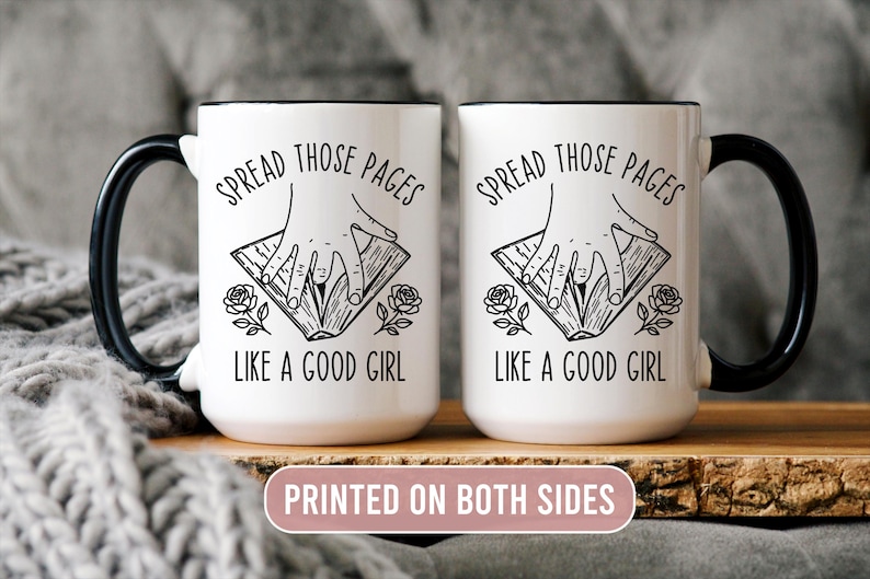 May include: Two white ceramic mugs with black handles and rims. Each mug features the text "SPREAD THOSE PAGES LIKE A GOOD GIRL" in black, along with a hand illustration and floral accents. The mugs are printed on both sides.