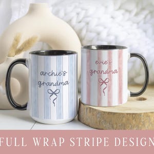 May include: Two ceramic mugs with black handles and rims. One mug has blue and white vertical stripes and the text "archie's grandma" with a bow graphic. The other mug has pink and white stripes and the text "evie's grandma" with a bow graphic. The mugs are on a wooden surface.